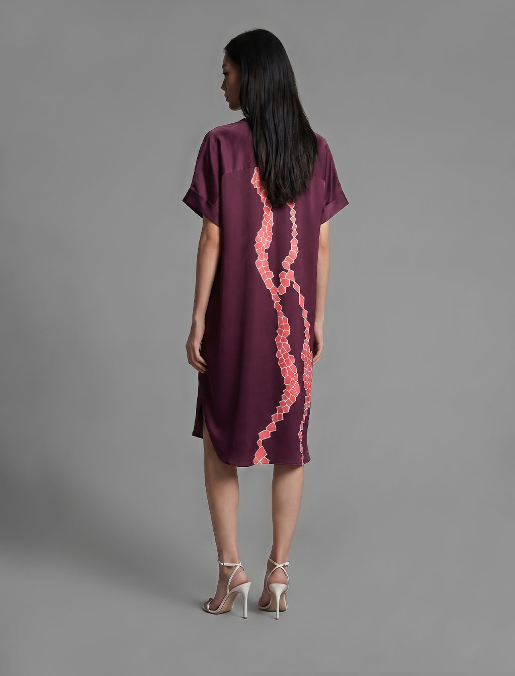 Back view. Mid length shirt dress in deep vino colour with contrasting bright pink graphic Macrosnake batik motif, featuring short sleeves with deep hem, curved hemline, simple collar with narrow V-neckline and relaxed contemporary silhouette.