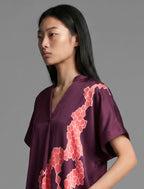 Neckline detail view. Mid length shirt dress in deep vino colour with contrasting bright pink graphic Macrosnake batik motif, featuring short sleeves with deep hem, curved hemline, simple collar with narrow V-neckline and relaxed contemporary silhouette.