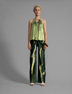 Front view. Silk satin halter top in fern green colour with elegant draping down the front, a high neckline anchored by a thin, grey silk cord that threads through the fabric, creating a V-shaped opening above the chest. Also draped at the back, the cord ties into a bow over a V-shaped opening. The hemline flows loosely over the hips.