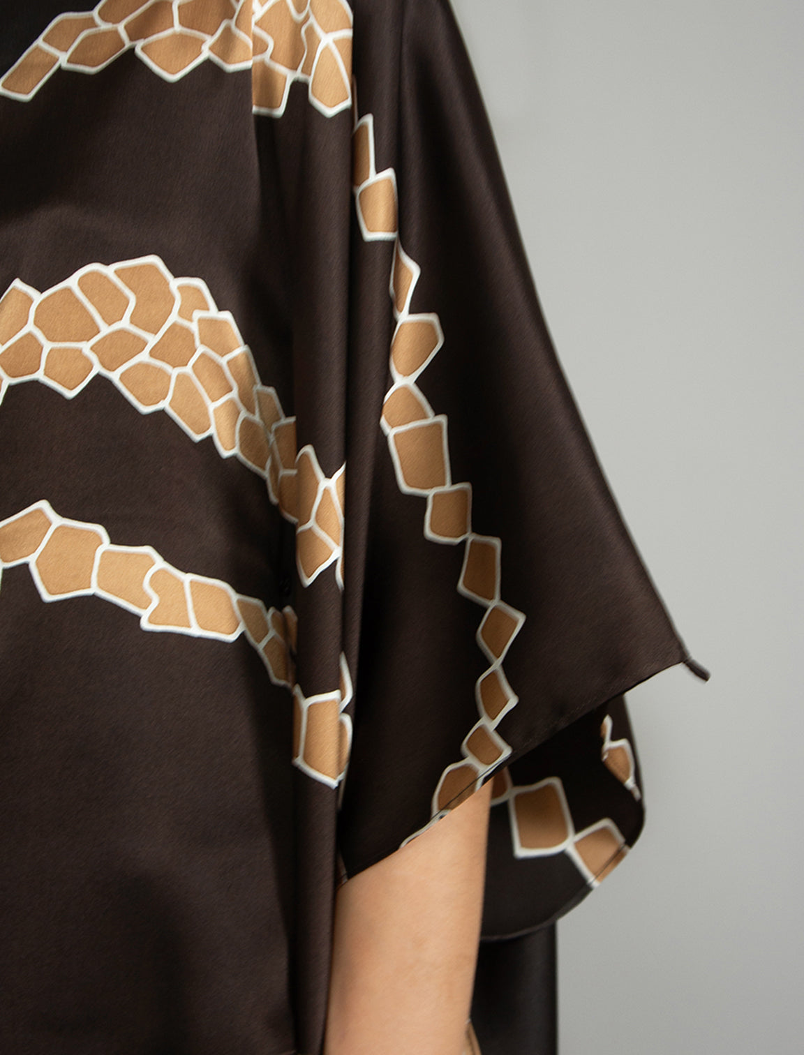 Sleeve detail: Flowing coffee colour silk top with graphic Macrosnake batik motif in warm beige tones, featuring fluid draped sleeves, asymmetrical hemline, and versatile contemporary silhouette designed to be worn three ways.
