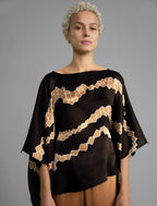Front view. Flowing coffee colour silk top with graphic Macrosnake batik motif in warm beige tones, featuring fluid draped sleeves, asymmetrical hemline, and versatile contemporary silhouette designed to be worn three ways.