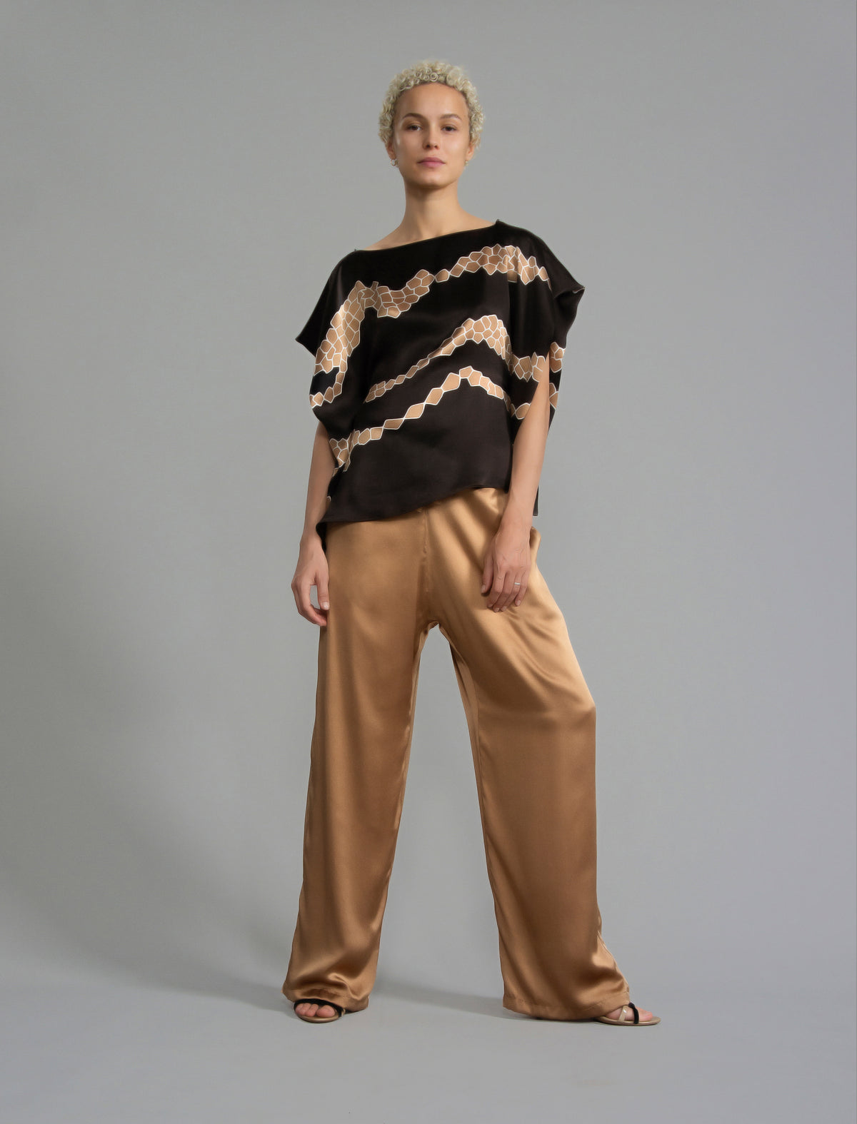 Short sleeve view. Flowing coffee colour silk top with graphic Macrosnake batik motif in warm beige tones, featuring fluid draped sleeves, asymmetrical hemline, and versatile contemporary silhouette designed to be worn three ways.