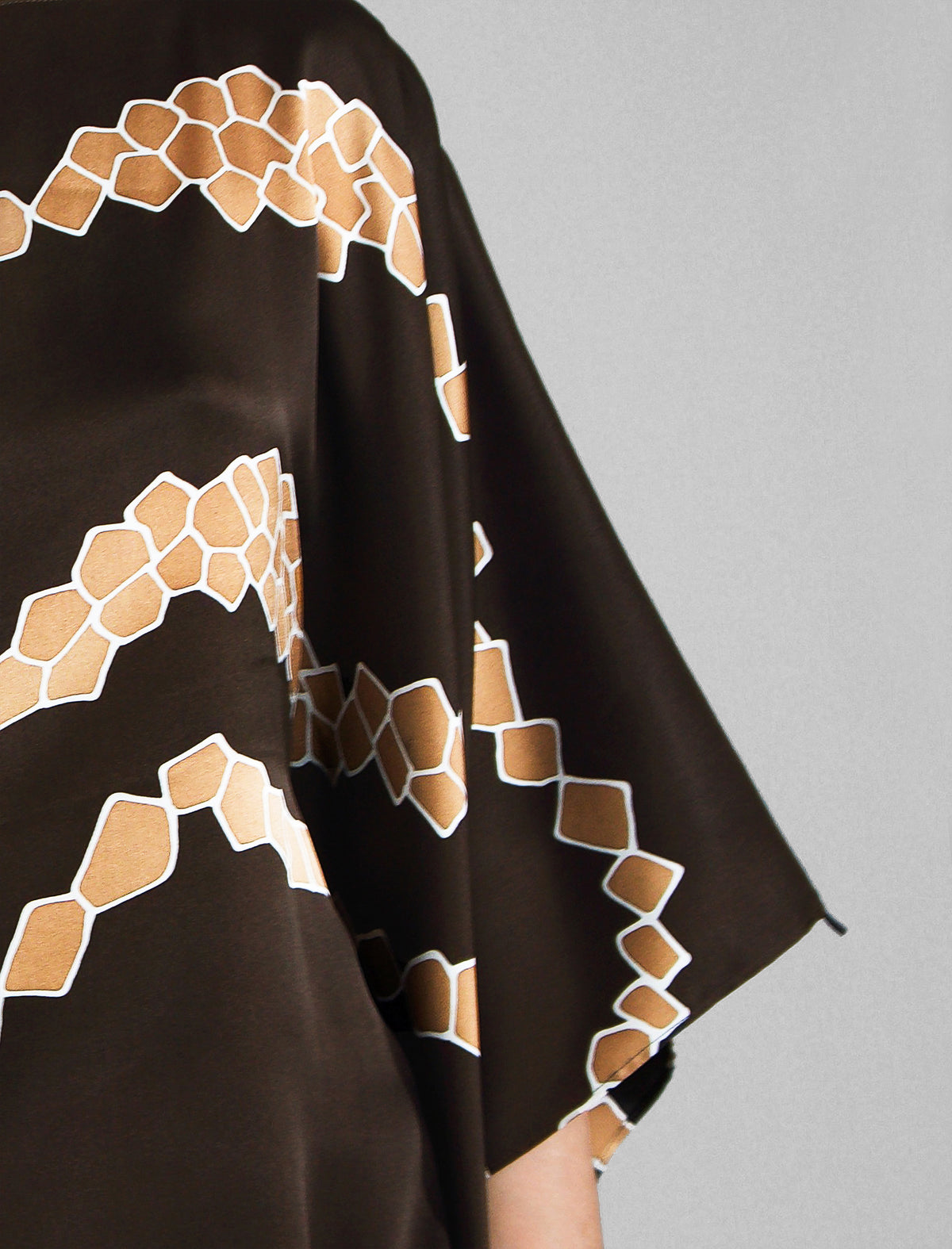 Sleeve detail. Flowing coffee colour silk top with graphic Macrosnake batik motif in warm beige tones, featuring fluid draped sleeves, asymmetrical hemline, and versatile contemporary silhouette designed to be worn three ways.
