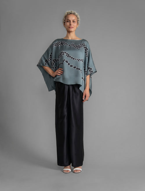 Full sleeve view. Flowing steel grey colour silk top with graphic Macrosnake batik motif in contrasting black, featuring fluid draped sleeves, asymmetrical hemline, and versatile contemporary silhouette designed to be worn three ways.