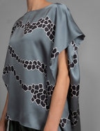 Folded sleeve detail. Flowing steel grey colour silk top with graphic Macrosnake batik motif in contrasting black, featuring fluid draped sleeves, asymmetrical hemline, and versatile contemporary silhouette designed to be worn three ways.