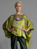 Front view. Flowing moss green colour silk top with graphic Macrosnake batik motif in contrasting green tone, featuring fluid draped sleeves, asymmetrical hemline, and versatile contemporary silhouette designed to be worn three ways.
