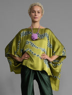 Front view. Flowing moss green colour silk top with graphic Macrosnake batik motif in contrasting green tone, featuring fluid draped sleeves, asymmetrical hemline, and versatile contemporary silhouette designed to be worn three ways.