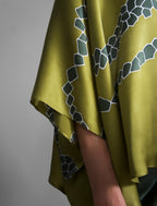 Sleeve detail: Flowing moss green colour silk top with graphic Macrosnake batik motif in contrasting green tone, featuring fluid draped sleeves, asymmetrical hemline, and versatile contemporary silhouette designed to be worn three ways.
