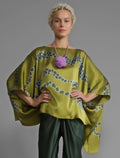 Front view. Flowing moss green colour silk top with graphic Macrosnake batik motif in contrasting green tone, featuring fluid draped sleeves, asymmetrical hemline, and versatile contemporary silhouette designed to be worn three ways.