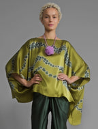 Front view. Flowing moss green colour silk top with graphic Macrosnake batik motif in contrasting green tone, featuring fluid draped sleeves, asymmetrical hemline, and versatile contemporary silhouette designed to be worn three ways.