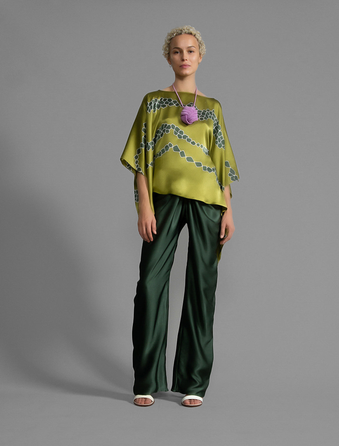 Variation 1. Flowing moss green colour silk top with graphic Macrosnake batik motif in contrasting green tone, featuring fluid draped sleeves, asymmetrical hemline, and versatile contemporary silhouette designed to be worn three ways.