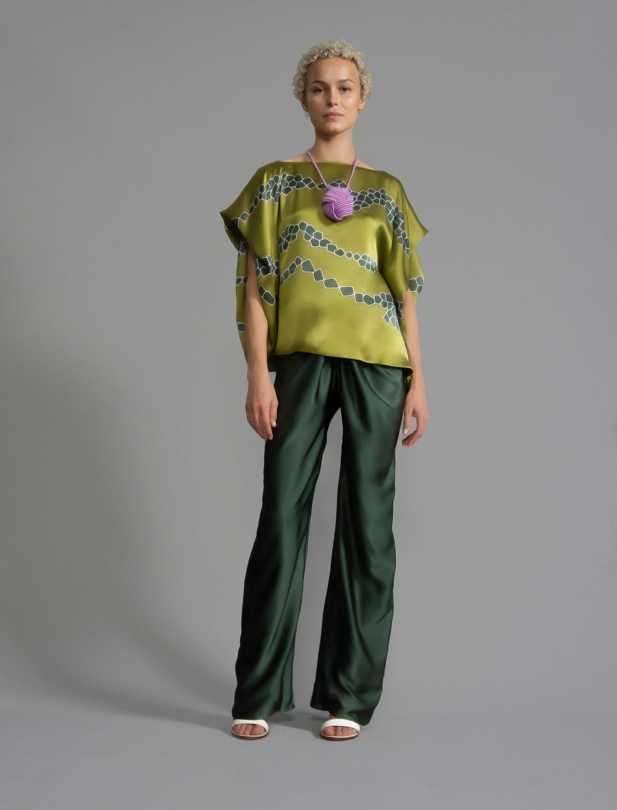 Variation 1. Flowing moss green colour silk top with graphic Macrosnake batik motif in contrasting green tone, featuring fluid draped sleeves, asymmetrical hemline, and versatile contemporary silhouette designed to be worn three ways.