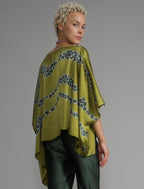 Back view. Flowing moss green colour silk top with graphic Macrosnake batik motif in contrasting green tone, featuring fluid draped sleeves, asymmetrical hemline, and versatile contemporary silhouette designed to be worn three ways.