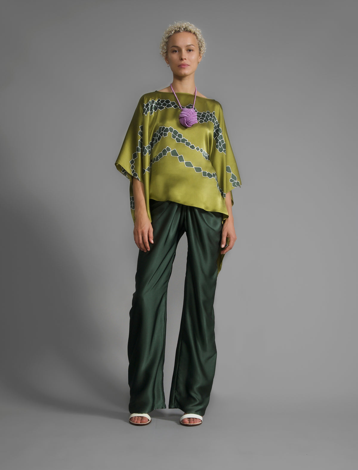 Variation 2. Flowing moss green colour silk top with graphic Macrosnake batik motif in contrasting green tone, featuring fluid draped sleeves, asymmetrical hemline, and versatile contemporary silhouette designed to be worn three ways.
