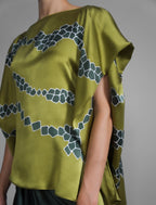 Short sleeve detail: Flowing moss green colour silk top with graphic Macrosnake batik motif in contrasting green tone, featuring fluid draped sleeves, asymmetrical hemline, and versatile contemporary silhouette designed to be worn three ways.