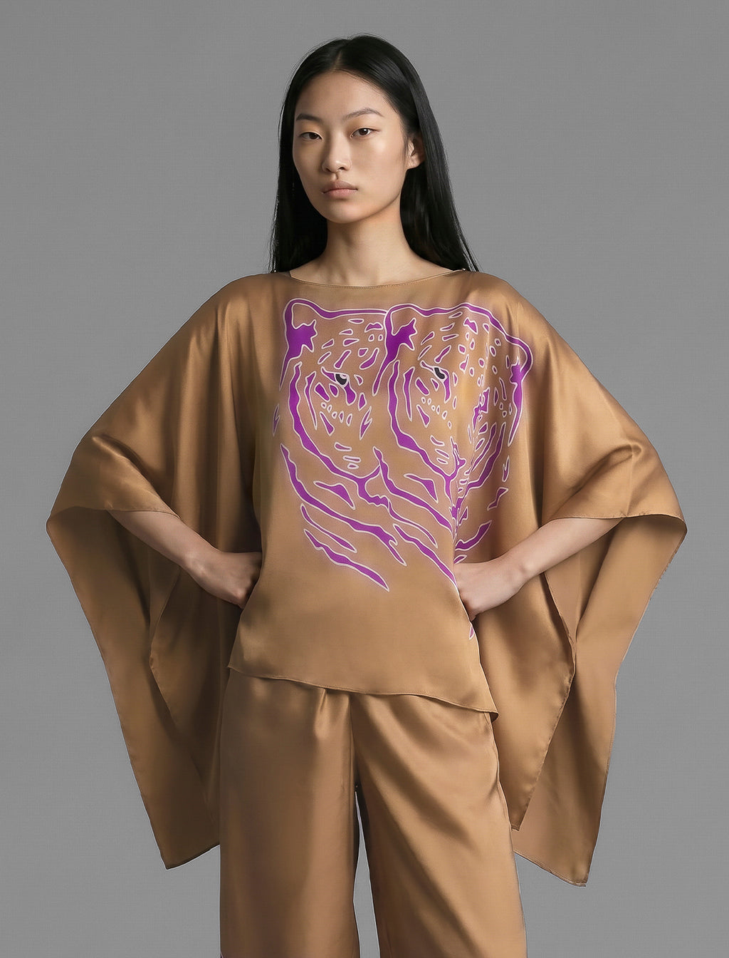 Front view. Flowing tobacco colour silk top with graphic Tiger batik motif in contrasting purple, featuring fluid draped sleeves, asymmetrical hemline, and versatile contemporary silhouette designed to be worn three ways.