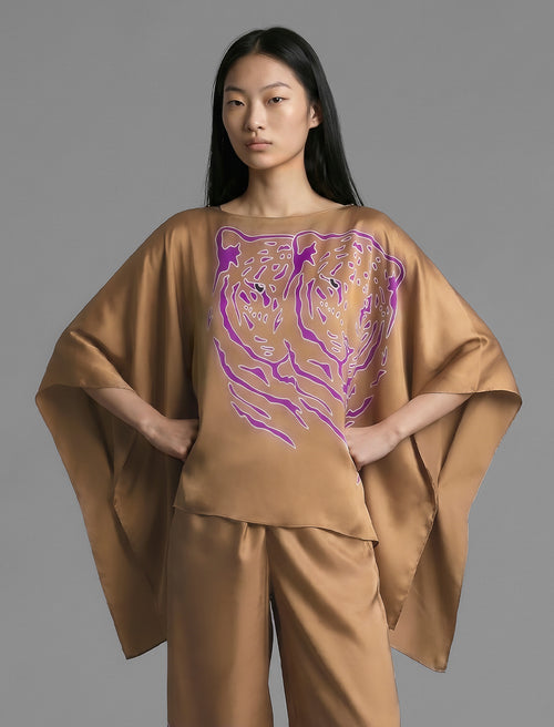 Front view. Flowing tobacco colour silk top with graphic Tiger batik motif in contrasting purple, featuring fluid draped sleeves, asymmetrical hemline, and versatile contemporary silhouette designed to be worn three ways.