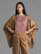 Front view. Flowing tobacco colour silk top with graphic Tiger batik motif in contrasting purple, featuring fluid draped sleeves, asymmetrical hemline, and versatile contemporary silhouette designed to be worn three wa