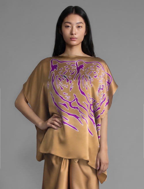 Folded sleeve view. Flowing tobacco colour silk top with graphic Tiger batik motif in contrasting purple, featuring fluid draped sleeves, asymmetrical hemline, and versatile contemporary silhouette designed to be worn three ways.