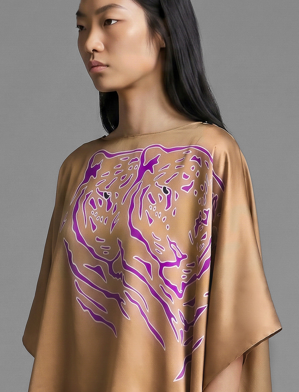 Motif detail view. Flowing tobacco colour silk top with graphic Tiger batik motif in contrasting purple, featuring fluid draped sleeves, asymmetrical hemline, and versatile contemporary silhouette designed to be worn three ways.