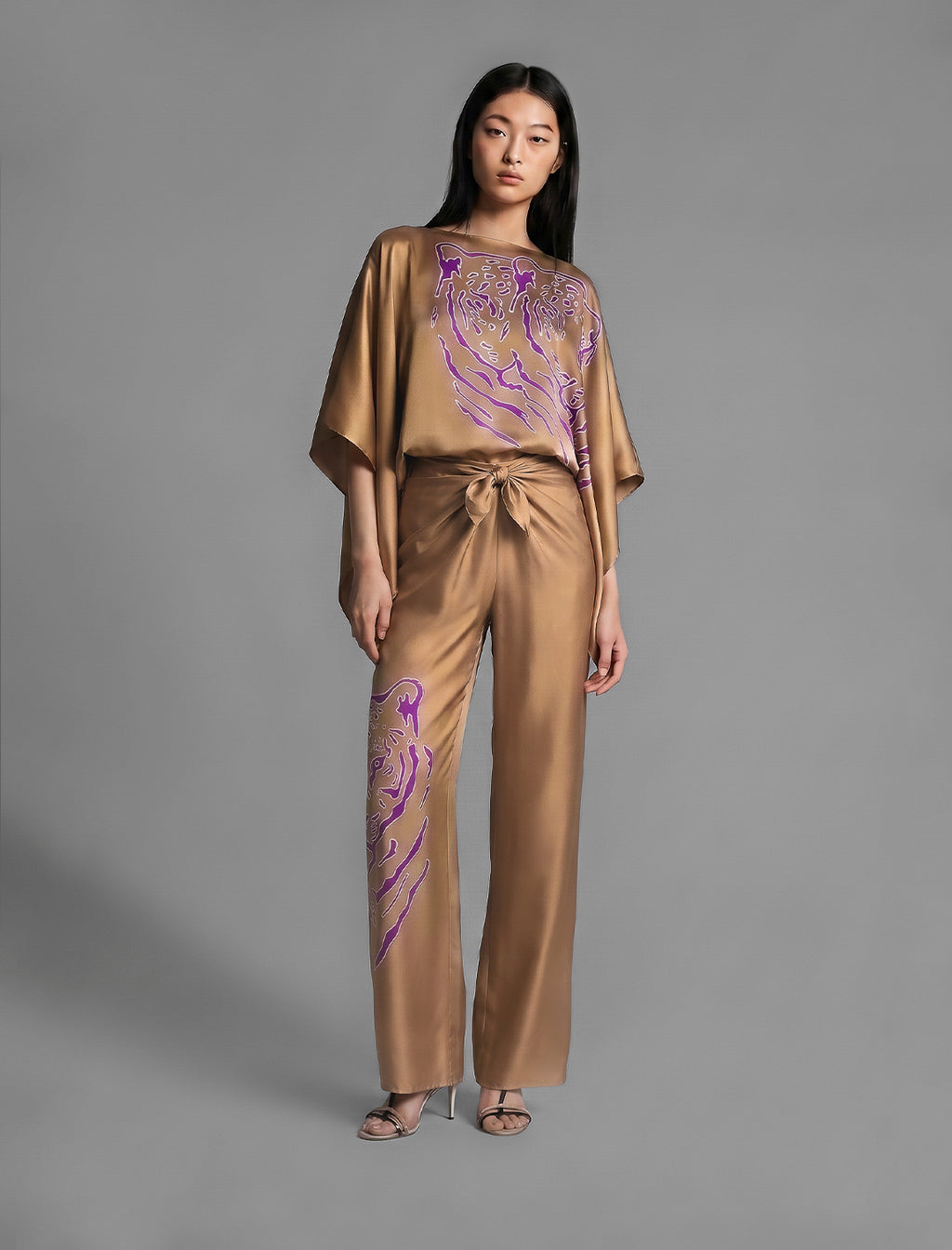 Full length view. Flowing tobacco colour silk top with graphic Tiger batik motif in contrasting purple, featuring fluid draped sleeves, asymmetrical hemline, and versatile contemporary silhouette designed to be worn three ways.
