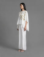 Full length view. Flowing white colour silk top with graphic Tiger batik motif in contrasting gold, featuring fluid draped sleeves, asymmetrical hemline, and versatile contemporary silhouette designed to be worn three ways.