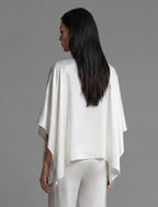 Back view. Flowing white colour silk top with graphic Tiger batik motif in contrasting gold, featuring fluid draped sleeves, asymmetrical hemline, and versatile contemporary silhouette designed to be worn three ways.