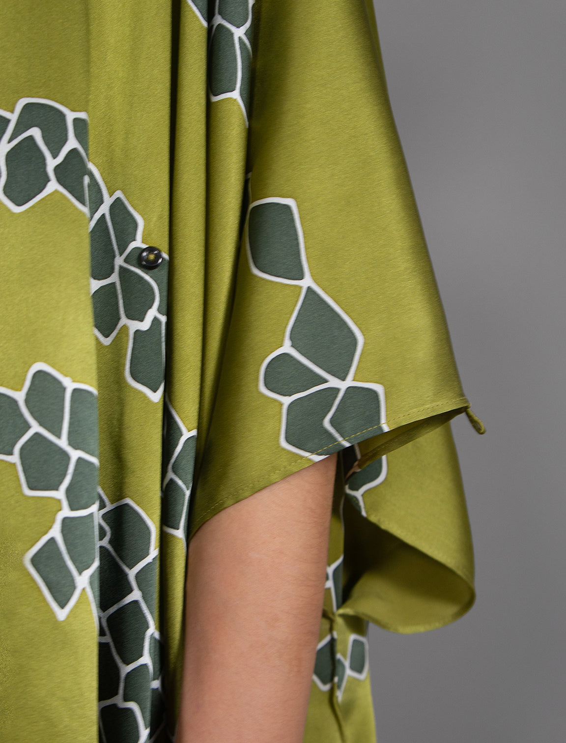 Sleeve detail: Flowing moss green colour silk top with graphic Macrosnake batik motif in contrasting green tone, featuring fluid draped sleeves, asymmetrical hemline, and versatile contemporary silhouette designed to be worn three ways.