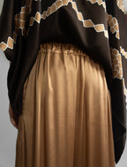 Gathered waistband detail: Relaxed wide-leg silk trousers in warm tobacco, featuring drawstring waistband, elasticated at the back. Soft gathered drape, fluid silhouette, and subtle lustrous finish.