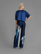 Back view. Long silk pants in blue navy colour with oversized tropical leaf batik motif, featuring a knot tie at the front and a slick relaxed silhouette.
