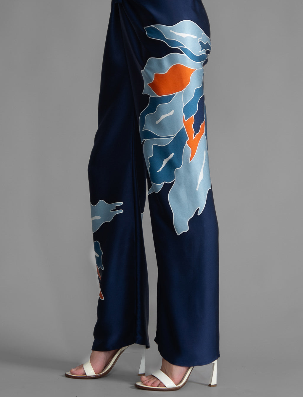 Motif detail view. Long silk pants in blue navy colour with oversized tropical leaf batik motif, featuring a knot tie at the front and a slick relaxed silhouette.