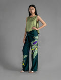 Side view. Long silk pants in teal colour with oversized tropical leaf batik motif, featuring a knot tie at the front and a slick relaxed silhouette.