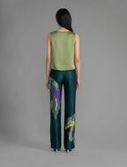 Back view. Long silk pants in teal colour with oversized tropical leaf batik motif, featuring a knot tie at the front and a slick relaxed silhouette.