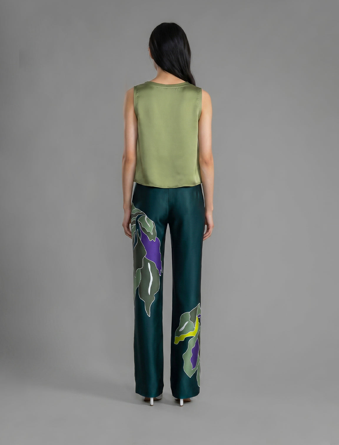 Back view. Long silk pants in teal colour with oversized tropical leaf batik motif, featuring a knot tie at the front and a slick relaxed silhouette.
