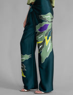 Motif detail. Long silk pants in teal colour with oversized tropical leaf batik motif, featuring a knot tie at the front and a slick relaxed silhouette.