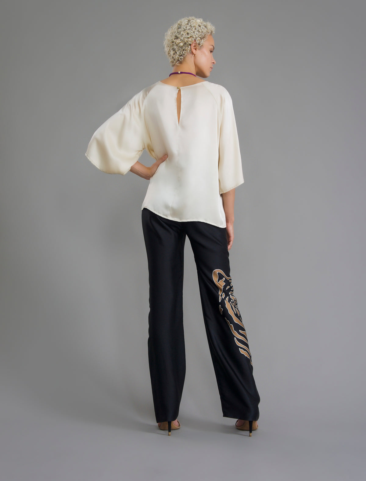 Back view. Long silk pants in black colour with tobacco tiger head batik motif, featuring a knot tie at the front and a slick relaxed silhouette. 