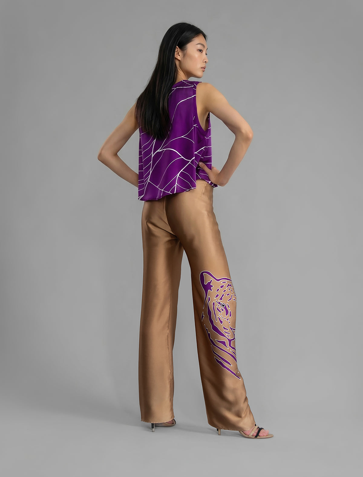 Back view. Long silk pants in tobacco colour with purple tiger head batik motif, featuring a knot tie at the front and a slick relaxed silhouette.