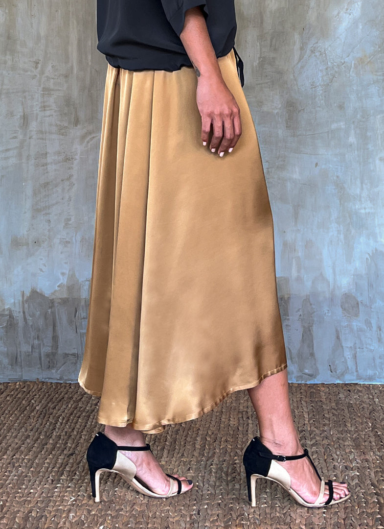Side detail: Quarzia Aline Skirt, flowing curved hemline gathered panel across the back-handcrafted from premium rayon. Plain Cashew-color crafted by artisans made in Bali.