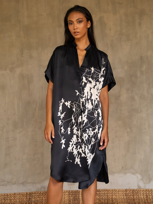  Loose fit for the  Robi silk satin dress, with handpainted batik pattern of leafy branches in white on black background. The short sleeves and V-neckline add a subtle structure to the soft and fluid silhouette.

