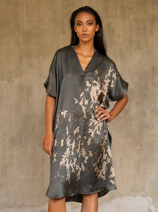  Loose fit for the  Robi silk satin dress, with handpainted batik pattern of leafy branches in beige on grey background. The short sleeves and V-neckline add a subtle structure to the soft and fluid silhouette.


