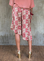 Back detail: this asymmetric Skirt-Pant is handcrafted from silk satin and blur the line between shorts and skirt. A deep, gathered waistband flows into a fluid silhouette, finished with a diagonal hemline that brings an unconventional edge to refined dressing.This  hand-painted stamp batik motif takes inspiration from the late 19th-century ‘Wiener Secession’ art movement, infusing the design with a refined sense of modularity. Pink and ivory colors here are beautifully matched.

