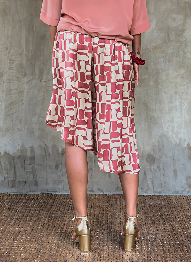 Back detail: this asymmetric Skirt-Pant is handcrafted from silk satin and blur the line between shorts and skirt. A deep, gathered waistband flows into a fluid silhouette, finished with a diagonal hemline that brings an unconventional edge to refined dressing.This  hand-painted stamp batik motif takes inspiration from the late 19th-century ‘Wiener Secession’ art movement, infusing the design with a refined sense of modularity. Pink and ivory colors here are beautifully matched.

