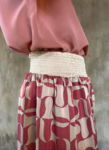Load image into Gallery viewer, Detail of elasticated waist: this asymmetric Skirt-Pant is handcrafted from silk satin and blur the line between shorts and skirt. A deep, gathered waistband flows into a fluid silhouette, finished with a diagonal hemline that brings an unconventional edge to refined dressing.This  hand-painted stamp batik motif takes inspiration from the late 19th-century ‘Wiener Secession’ art movement, infusing the design with a refined sense of modularity. Pink and ivory colors here are beautifully matched.
