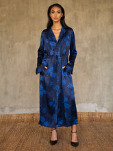 Load image into Gallery viewer, Hand-crafted in glossy pure silk, this jacket&#39; neck-line dress it has elegant, structured trumpet cuffs,   discreet pockets and waist drawstring add to the sophistication and comfort. Pure silk decorated by hand with our leafy pattern Dedaun, in rich blue tones.
