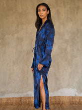 Load image into Gallery viewer, Side detail: hand-crafted in glossy pure silk, this jacket&#39; neck-line dress it has elegant, structured trumpet cuffs,   discreet pockets and waist drawstring add to the sophistication and comfort. Pure silk decorated by hand with our leafy pattern Dedaun, in rich blue tones.
