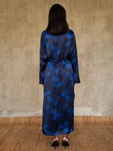 Load image into Gallery viewer, Back detail: hand-crafted in glossy pure silk, this jacket&#39; neck-line dress it has elegant, structured trumpet cuffs,   discreet pockets and waist drawstring add to the sophistication and comfort. Pure silk decorated by hand with our leafy pattern Dedaun, in rich blue tones.
