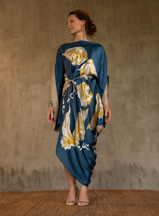 Asymmetric long dress in deep royale moroccan blue background and floral pattern in beige and gold. Rich beige border on the kimono-like sleeves.Luxury resort-wear in silk batik made in Bali. 