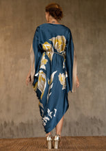 Load image into Gallery viewer, Back detail: asymmetric long dress in deep royale moroccan blue background and floral pattern in beige and gold. Rich beige border on the kimono-like sleeves.Luxury resort-wear in silk batik made in Bali. 
