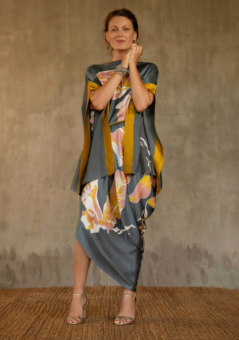 Asymmetric long dress in grey steel background and floral pattern in pink and gold. Deep gold border on the kimono-like sleeves.Luxury resort-wear in silk batik made in Bali. 