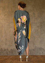 Load image into Gallery viewer, Back detail: asymmetric long dress in grey steel background and floral pattern in pink and gold. Deep gold border on the kimono-like sleeves. Luxury resort-wear in silk batik made in Bali.
